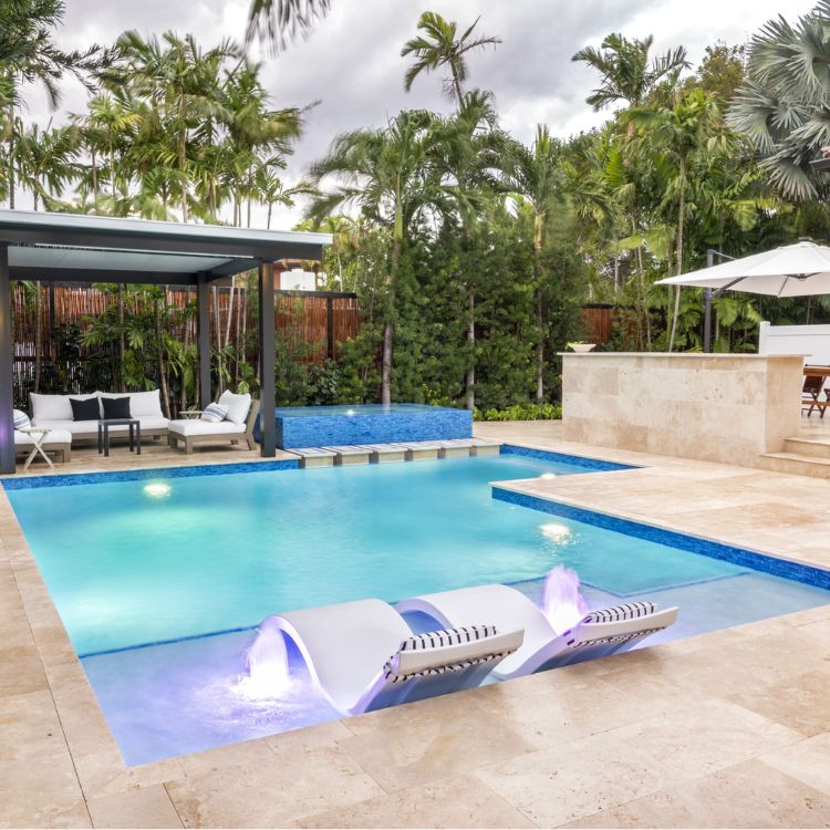 Luxury backyard pool with built-in loungers, spa, and tropical landscaping